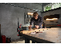 Homme ponçant une planche de bois avec une ponceuse excentrique dans un atelier.