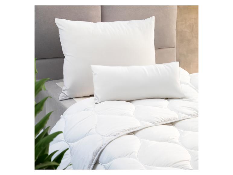 Oreillers et couette blancs sur un lit avec tête de lit grise.