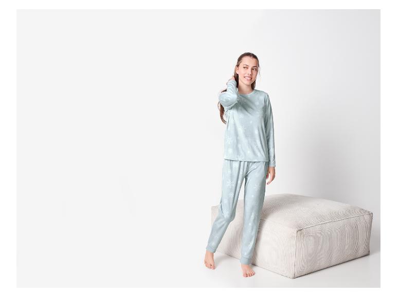 Femme en pyjama bleu clair à motif de flocons de neige, debout près d'un pouf.