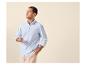Homme en chemise rayée bleue et pantalon beige, tenant des lunettes.