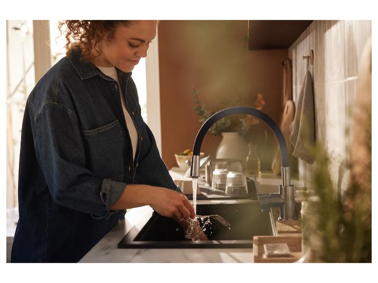 Une femme fait la vaisselle dans la cuisine sous un robinet moderne.
