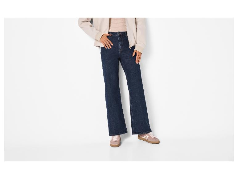 Femme en jean évasé bleu foncé, veste beige et baskets roses