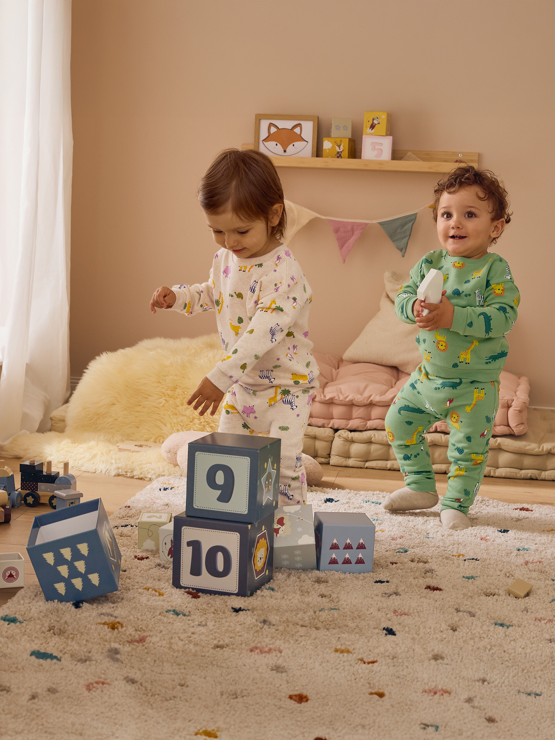 Deux enfants en pyjama à motifs animaux jouent avec des blocs dans une chambre.