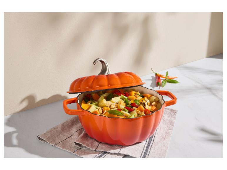 Cocotte orange en forme de citrouille remplie de légumes et de fruits, couvercle entrouvert.