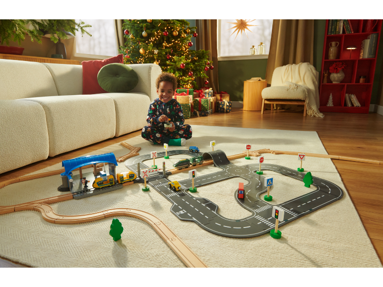 Enfant jouant avec un train en bois et un tapis de route sur un tapis dans un salon festif.