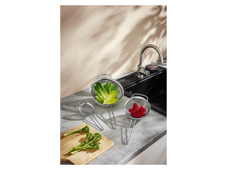 Ensemble de passoires pour laver la laitue et les framboises, avec du brocoli sur une planche près de l'évier.