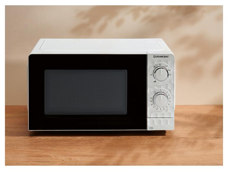 Micro-ondes blanc sur une table en bois avec deux boutons rotatifs et réglages de puissance.