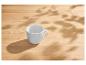 Une tasse blanche vide sur une table en bois avec des ombres de feuilles.