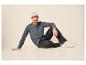 Homme en chemise henley grise, jean noir et baskets blanches assis par terre.