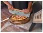 Personne coupant une pizza fraîchement cuite avec un grand couteau à pizza sur une planche en bois.