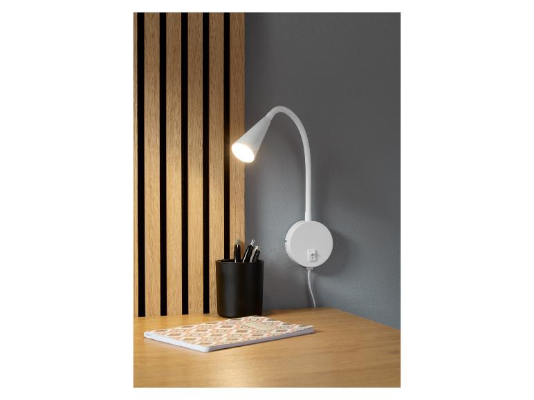 Une lampe murale blanche avec un bras flexible sur un bureau en bois avec un carnet.