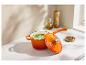 Marmite en fonte orange avec soupe verte, huile d'olive et épices sur un comptoir blanc.