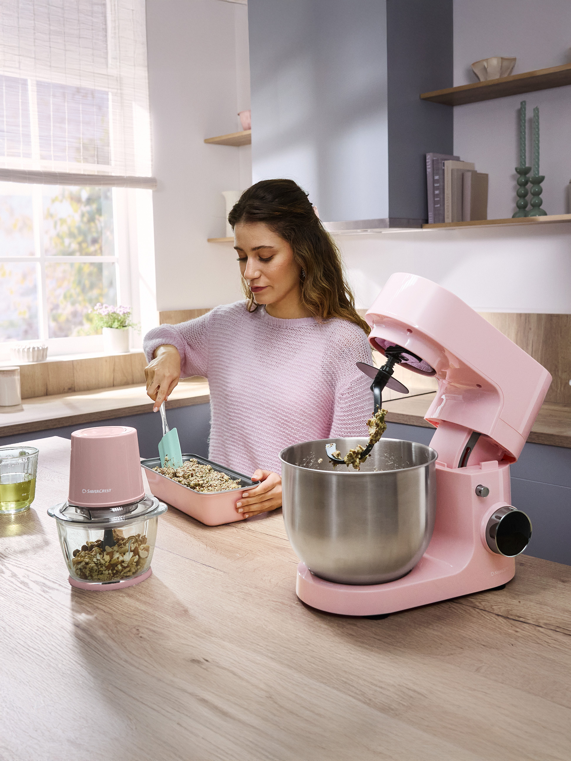 Femme préparant des céréales avec un robot pâtissier rose et un hachoir.