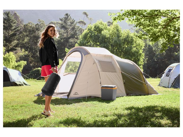 Femme avec sac de camping et tente sur un camping herbeux.