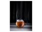 Théière en verre avec du thé infusé et de la vapeur s'élevant sur un fond sombre.