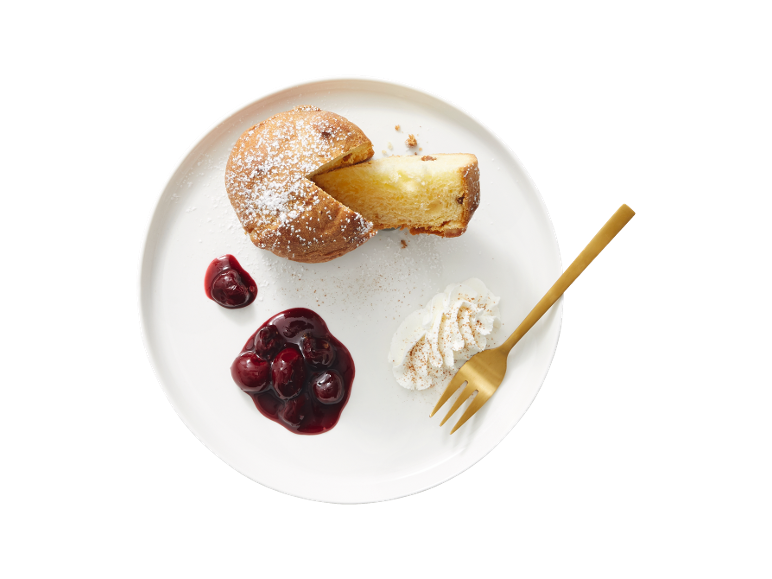 Gâteau saupoudré de sucre glace, compote de cerises et crème fouettée sur une assiette blanche.