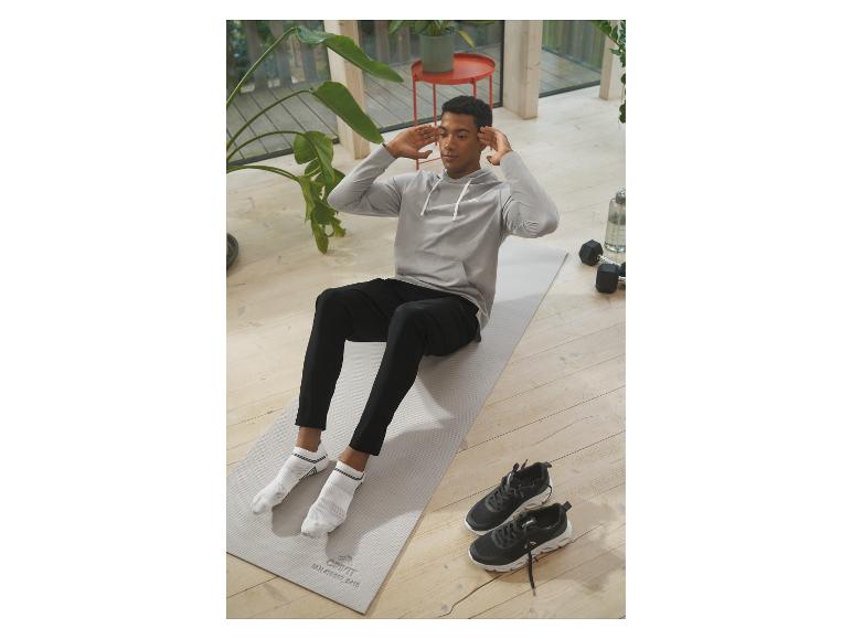 Un homme faisant des abdominaux sur un tapis de yoga, avec des baskets et des haltères à côté.