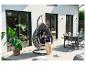 Femme lisant dans un fauteuil suspendu sur une terrasse avec table à manger et plantes.