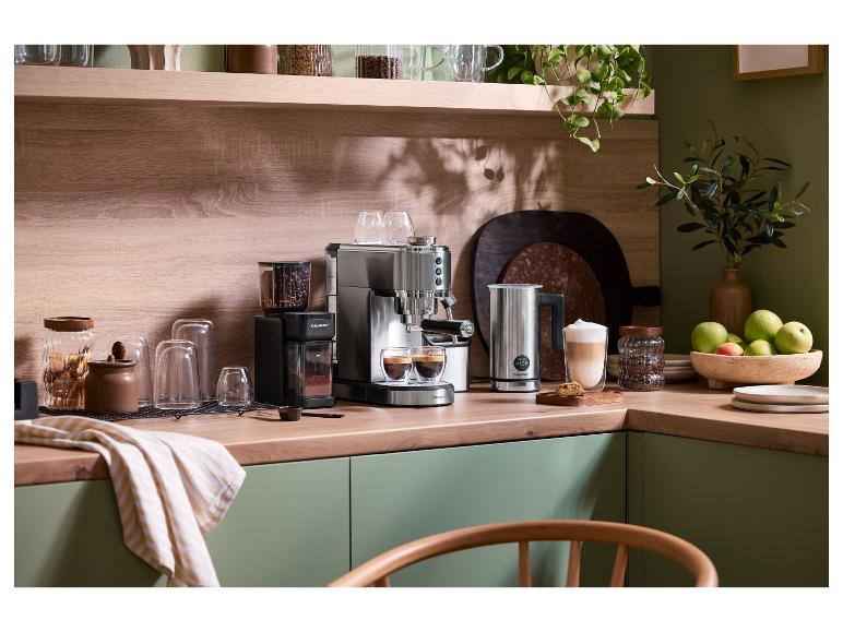 Machine à café et moulin sur un comptoir en bois avec des armoires vertes et des plantes.