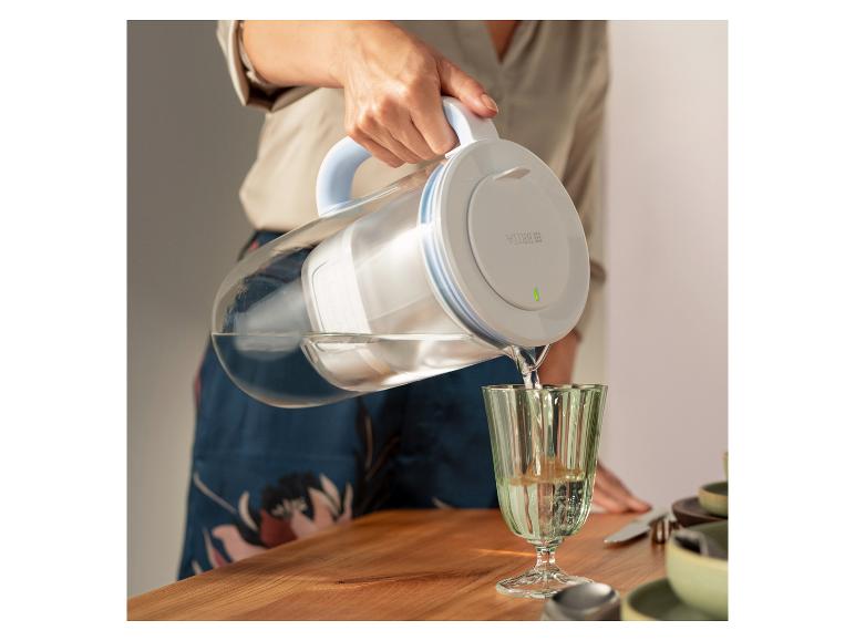 Carafe filtrante en verre BRITA versant de l'eau dans un verre sur une table.