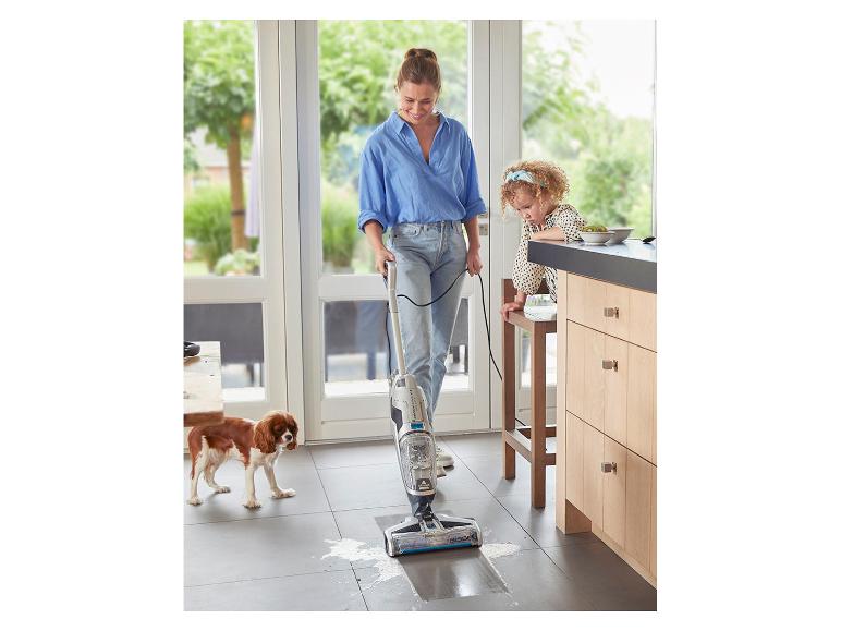 Femme nettoyant un sol de cuisine avec un aspirateur eau et poussière, enfant et chien à proximité.