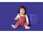 Bébé heureux en barboteuse tricotée rose assis à côté d'un cube bleu.
