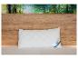Un oreiller blanc matelassé avec une étiquette bleue Beco repose sur un lit avec une tête de lit en bois et un papier peint forêt.