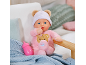 Poupée bébé souple en pyjama rose et bonnet avec oreilles d'ours à côté d'un biberon.