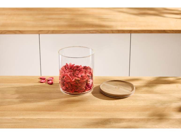 Bocal en verre avec des fraises déshydratées et un couvercle en bois sur un plan de travail.