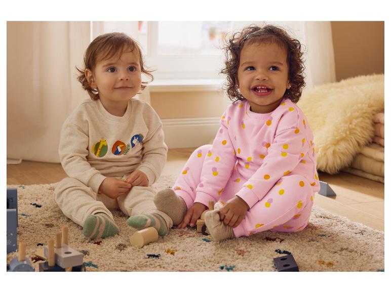 Deux tout-petits en pyjamas assortis sont assis sur un tapis et jouent avec des jouets en bois.