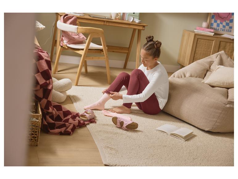 Fille enfilant des chaussettes roses sur le sol, avec des sandales et un livre.