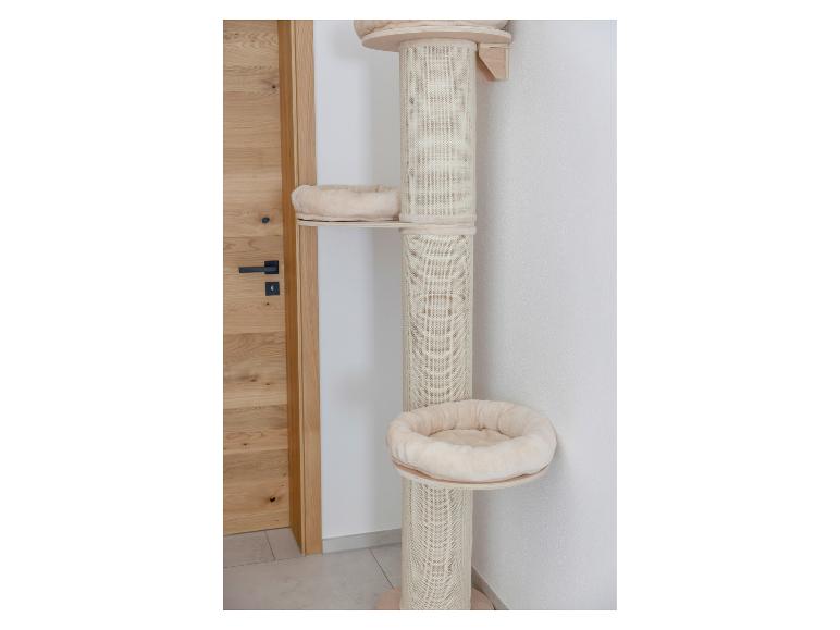 Arbre à chat beige avec plusieurs plateformes et lits douillets, à côté d'une porte en bois.