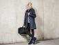 Une femme porte un imperméable bleu, un sac noir et des bottes de pluie bleues.
