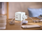 Multiprise blanche cubique avec ports USB et prises, chargeant des appareils sur une table en bois.