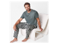 Un homme assis sur un fauteuil moelleux, vêtu d'un t-shirt vert foncé et d'un pantalon à motifs.