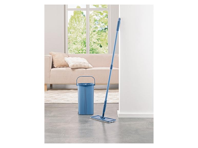 Seau et balai à franges bleus dans un salon lumineux avec canapé et fenêtre.