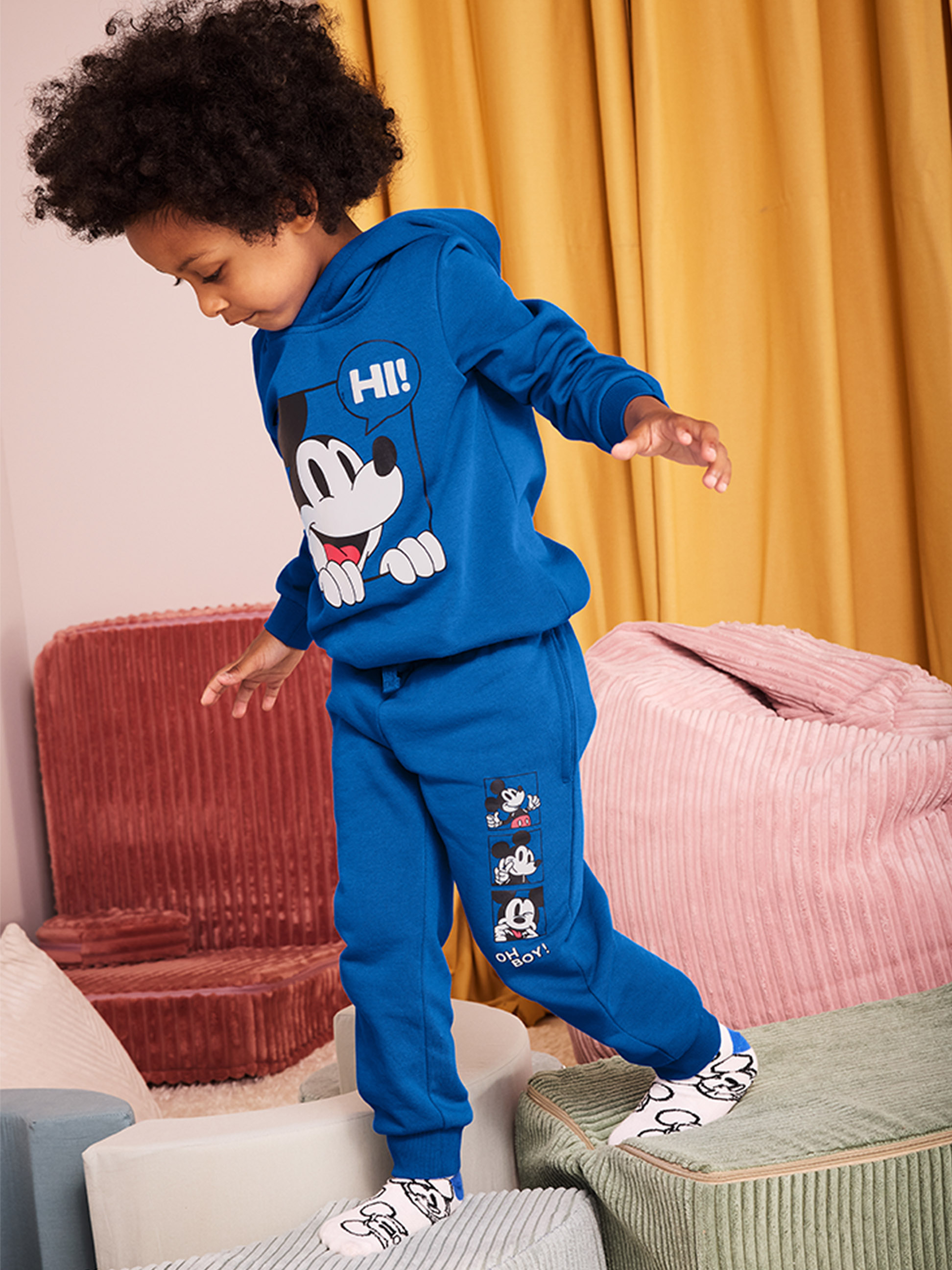 Un enfant en sweat à capuche et pantalon de survêtement bleu Mickey Mouse marche sur des blocs souples.
