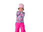 Fille souriante avec un bonnet rose, un haut à motifs et un pantalon de ski fuchsia.