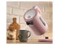 Bouilloire rose versant de l'eau chaude dans une tasse de thé sur un comptoir en bois.
