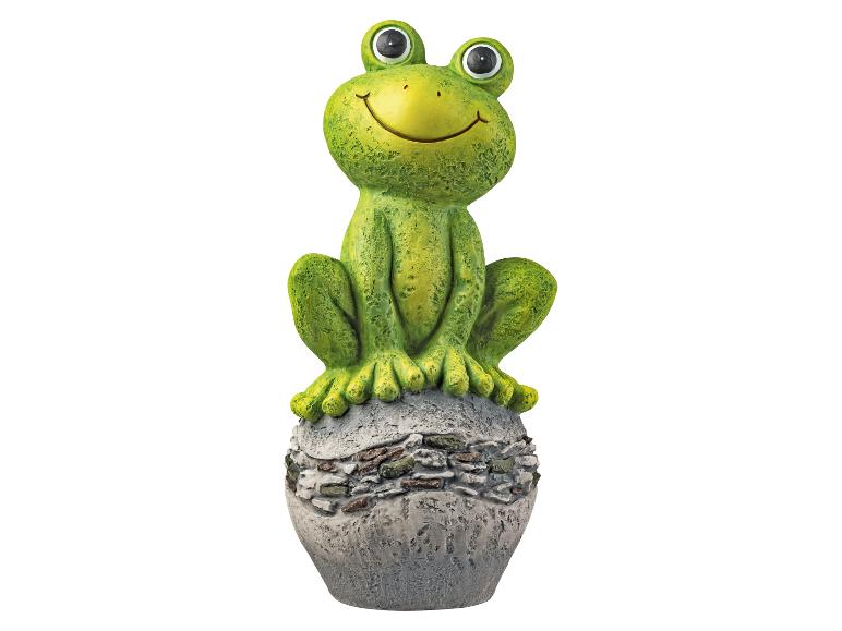 Figurine de grenouille verte souriante assise sur une base grise texturée.