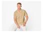 Homme en chemise beige à manches courtes et pantalon blanc, assis sur un fond blanc.