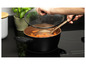 Une casserole noire avec un couvercle et une louche pleine de carottes, sur une plaque à induction.