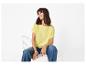 Femme en t-shirt jaune et jean bleu, assise sur une chaise blanche.