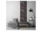 Un salon moderne avec un accent de papier peint floral foncé, une couverture rayée grise et un lampadaire noir.