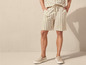Un homme porte un short en lin rayé et des baskets beiges.