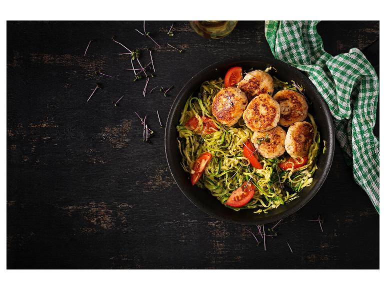 Galettes de poulet avec nouilles de courgettes et tomates dans une poêle noire.