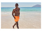 Homme en short de bain orange marchant sur la plage.