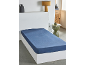Drap-housse bleu sur un lit blanc dans une chambre avec table de chevet et lampe.