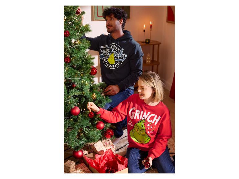 Un couple décore un sapin de Noël avec des sweats à capuche sur le thème du Grinch.