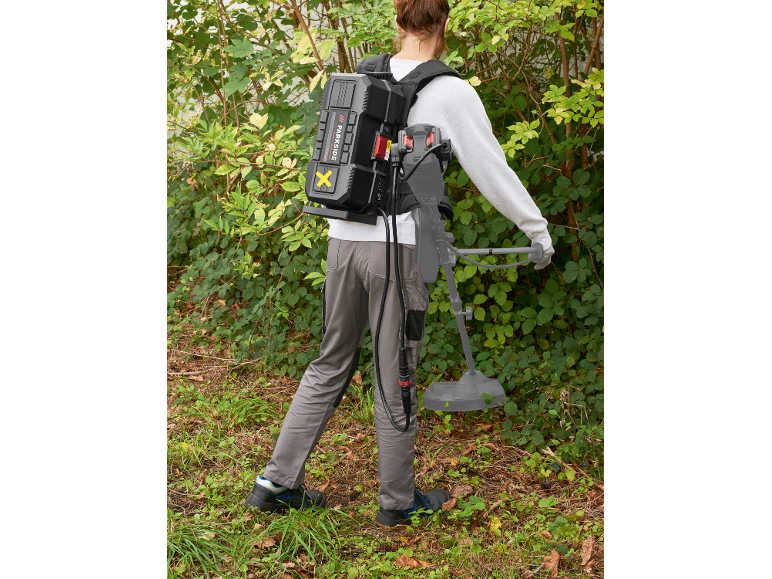 Personne avec batterie dorsale et coupe-bordure dans un jardin.